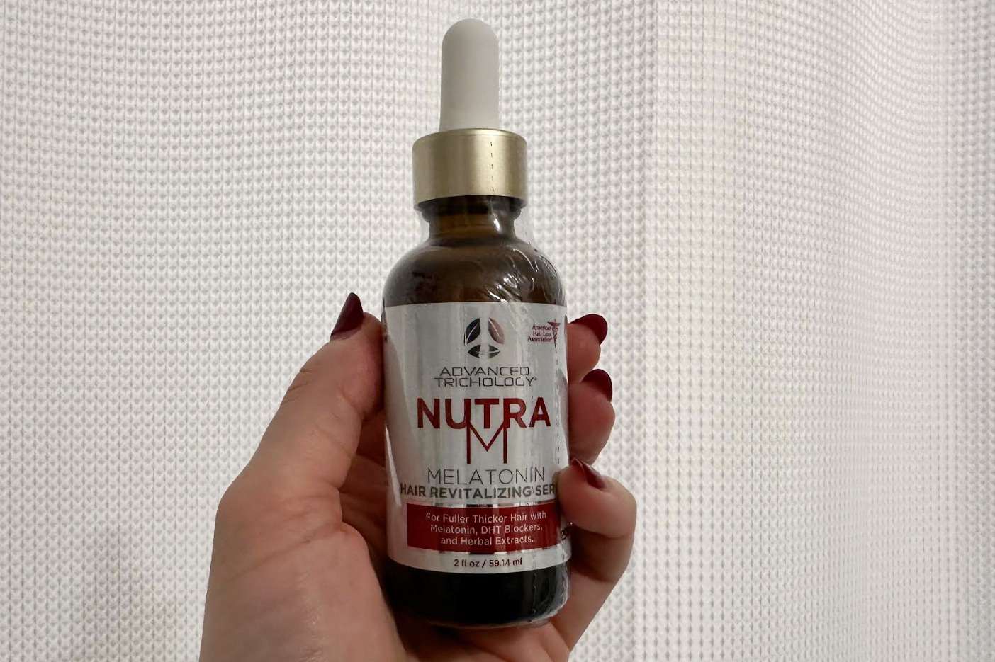 A person holds up a bottle of Advanced Trichology NutraM Topical Melatonin Hair Growth Serum