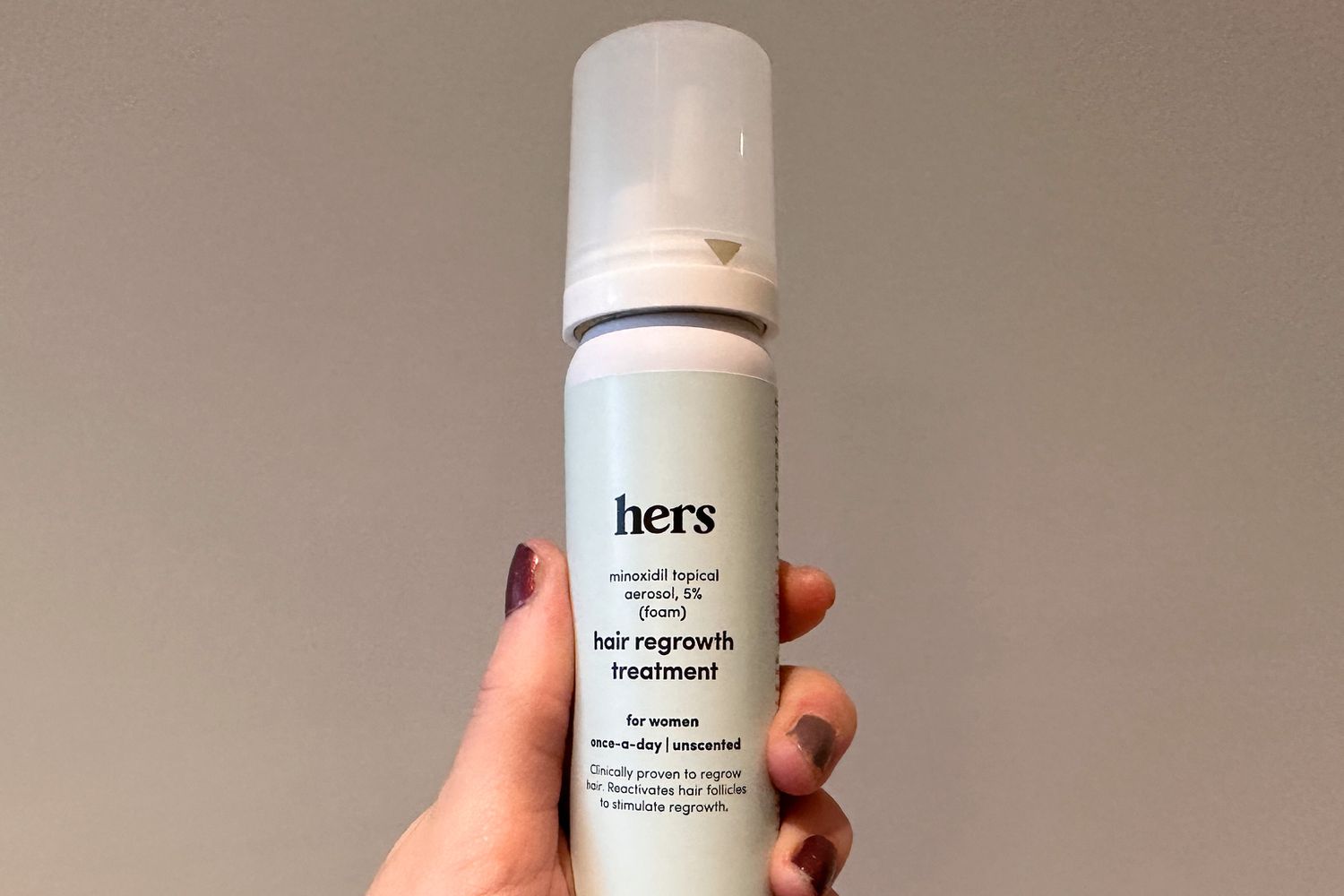 A person holds up a bottle of hers Minoxidil Foam for Women