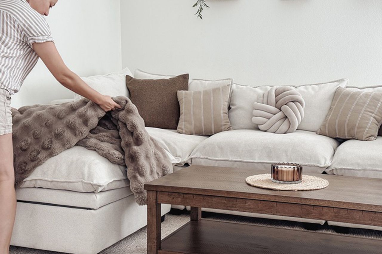 Person arranging a blanket on a sectional sofa in a contemporary living room People