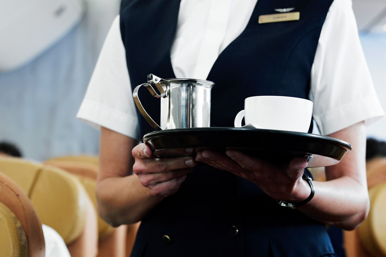 Flight attendant holding tray with coffee, mid section A flight attendant serves coffee.Credit: Getty