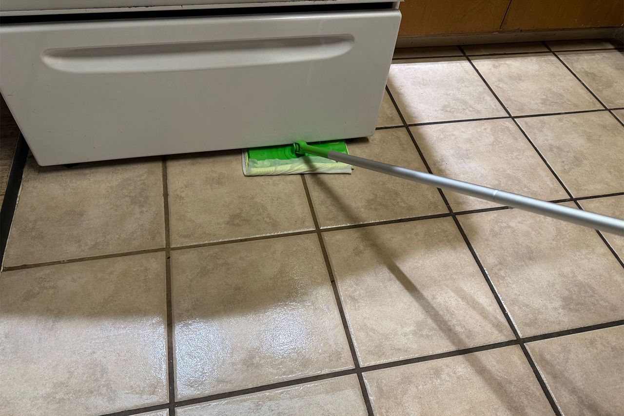 A Swiffer mop cleaning tile flooring near the base of an appliance Credit: People