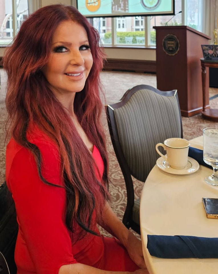 A woman seated at a table indoors smiling wearing a formal outfit Credit: Jayne Black