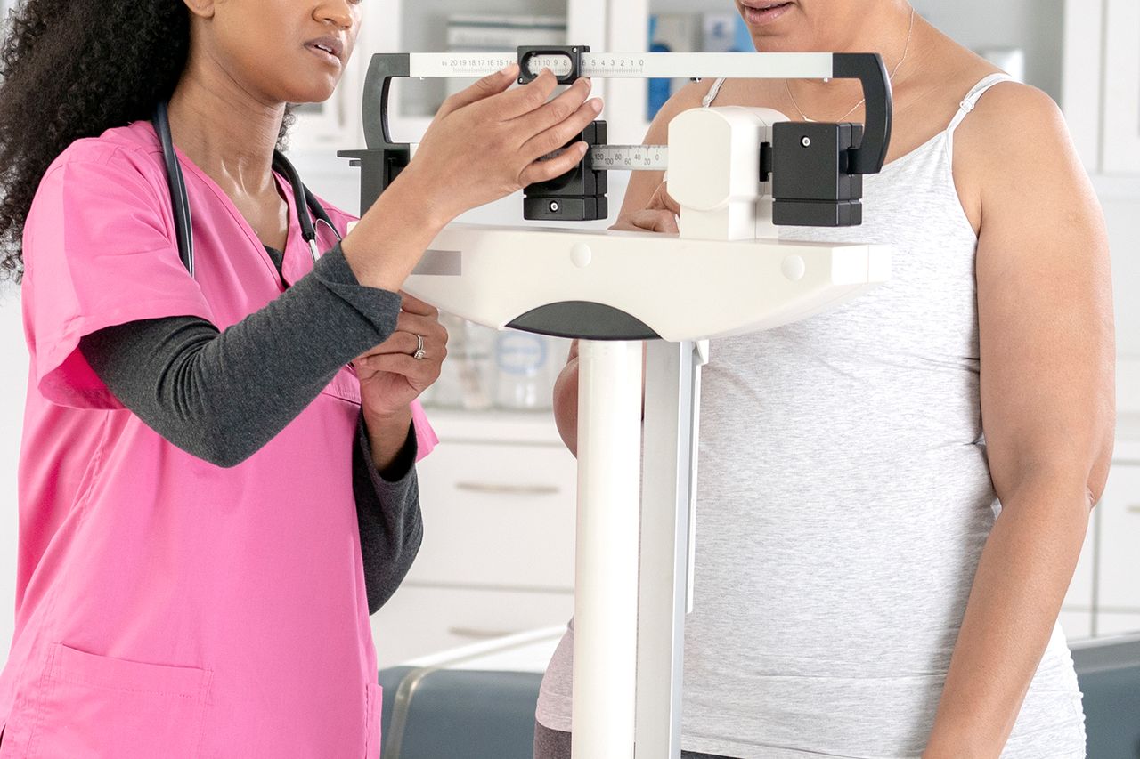 A healthcare professional adjusting a balance scale to measure a patients weight Stock image of a patient being weighed in a doctor's officeCredit: Getty