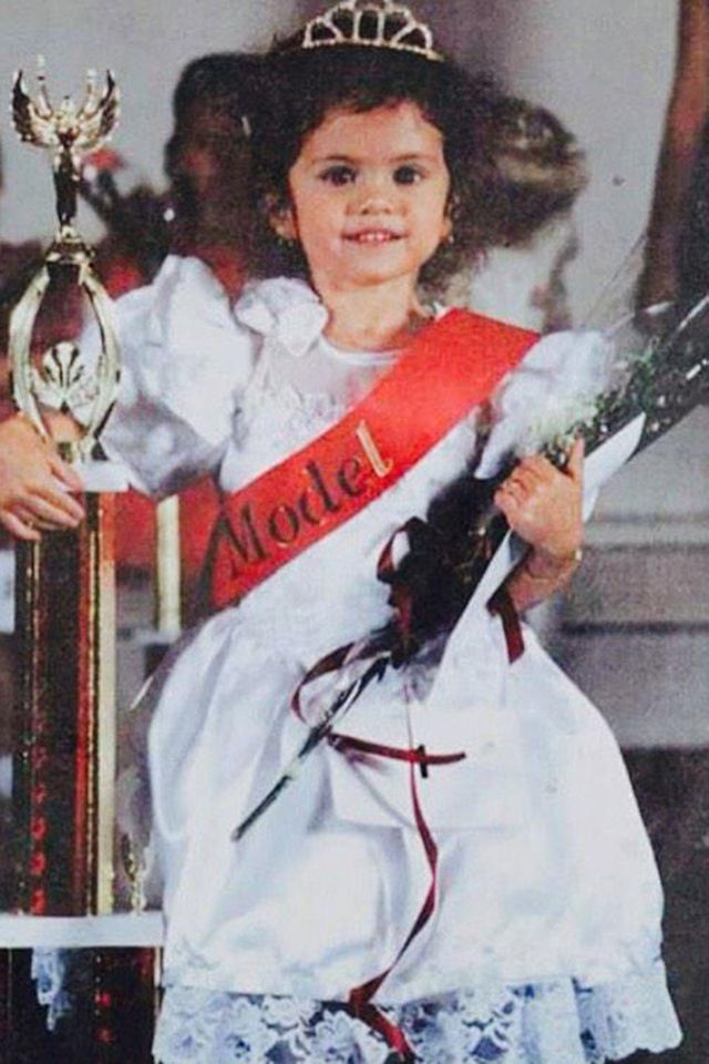 A young Selena Gomez wears a white dress while posing with a pageant trophy, flowers and a gold tiara after a pageantCredit: Selena Gomez/X
