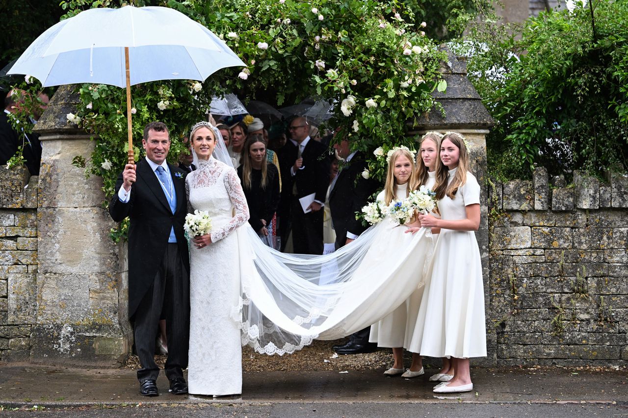 A wedding couple standing outside under an umbrella while the brides train is held by three bridesmaids in white dresses Peter Phillips and Harriet SperlingCredit: Samir Hussein/WireImage