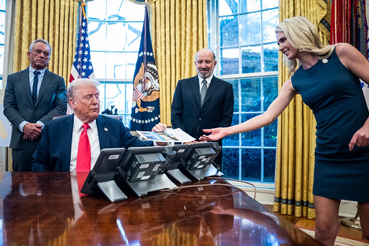 Natalie Harp hands President Donald Trump a document as he is flanked by Health and Human Services Secretary Robert F. Kennedy Jr. and Commerce Secretary Howard Lutnick.Credit: Jabin Botsford/The Washington Post via Getty